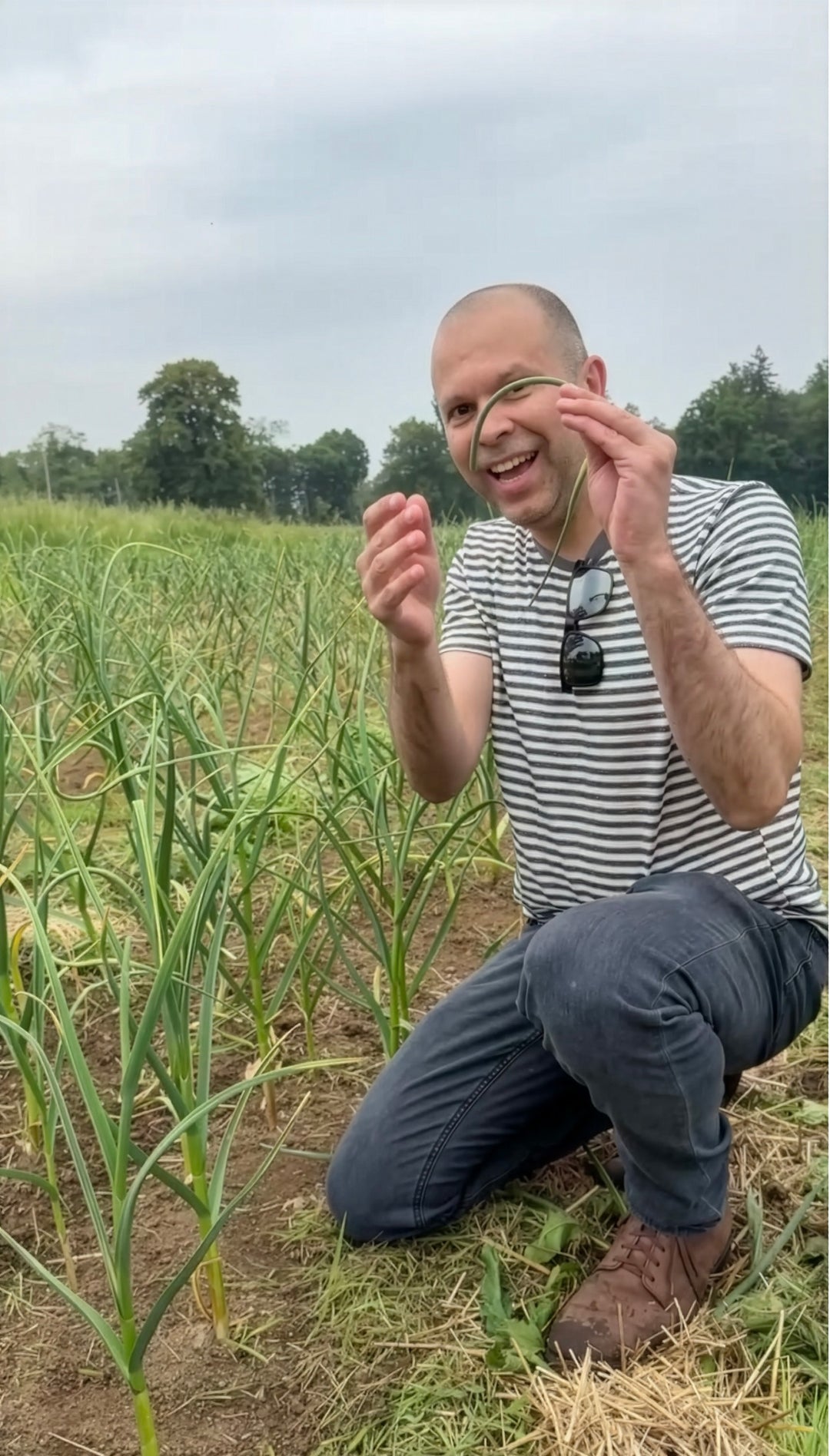 Ketan holding garlic scapes in the field