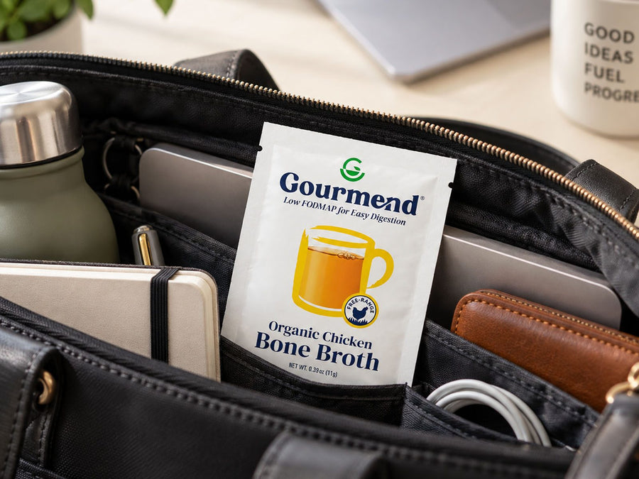 A packet of Gourmend chicken bone broth powder tucked into a work bag beside a laptop, notebook and water bottle