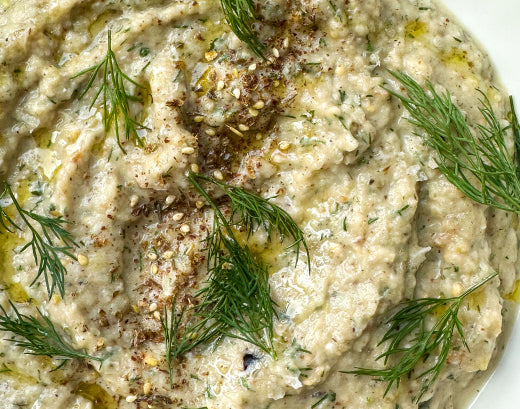 A close-up of a creamy dip swirled with olive oil, fresh dill and cracked spice