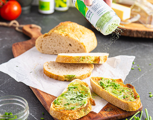 Garlic Scape Powder being shaken over slices of toasted sourdough spread with herb butter, on a wooden board