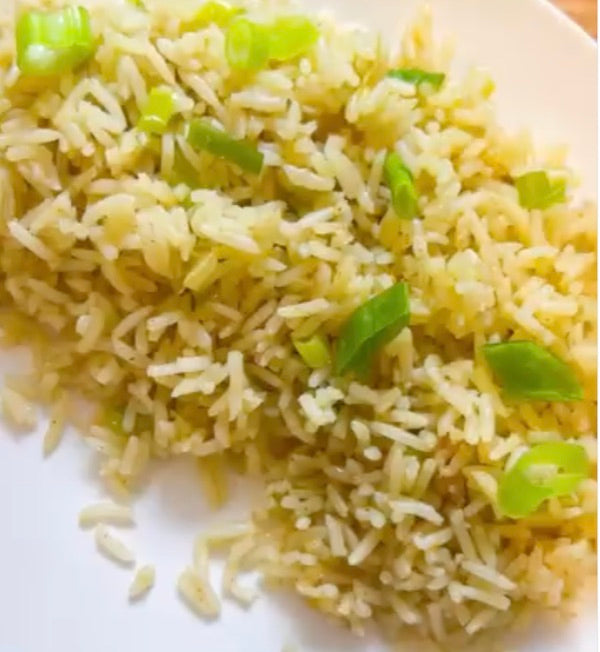 A plate of long-grain rice flecked with herbs and scattered with sliced green onion tops