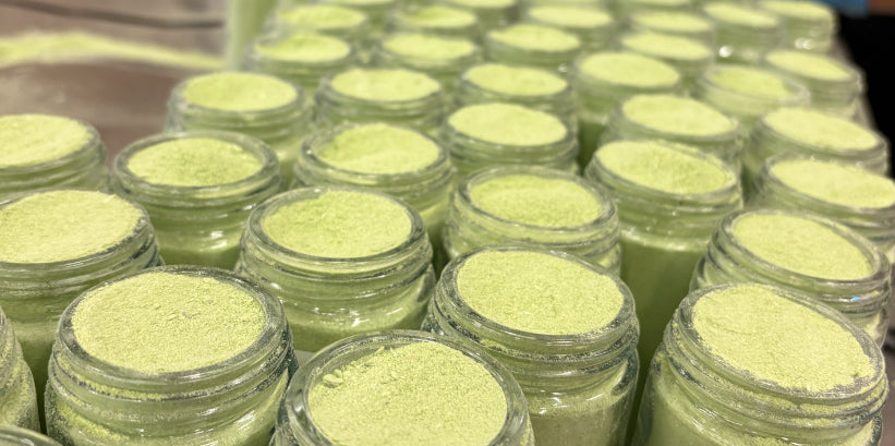 Rows of open glass jars filled with pale green garlic scape powder