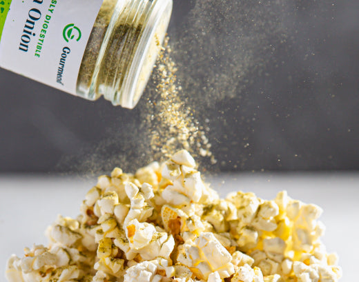 A jar of Gourmend Green Onion Powder being shaken over a pile of popcorn