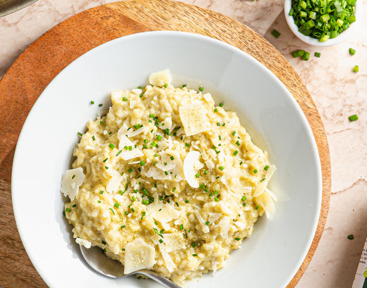 A bowl of creamy risotto topped with shaved parmesan and chopped chives