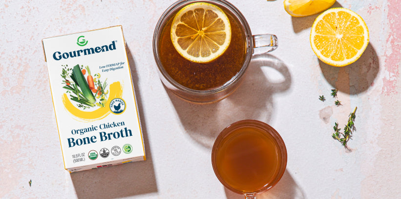 Overhead view of a broth carton, a mug of broth with a lemon slice, and fresh thyme