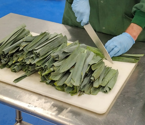 Hands slicing a board of organic leek greens with a chef's knife